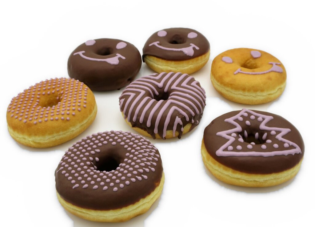 Seven doughnuts decorated with lilac smileys, dots, chevron lines and a tree