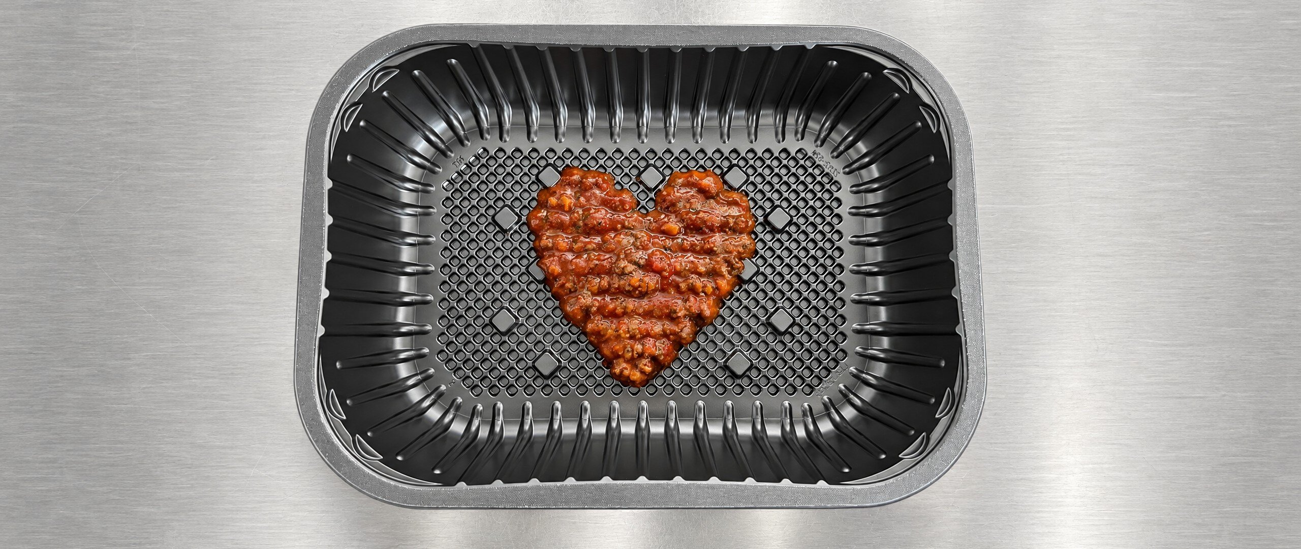 Bolognese meat sauce deposited in a heart shape in a black ready meal tray