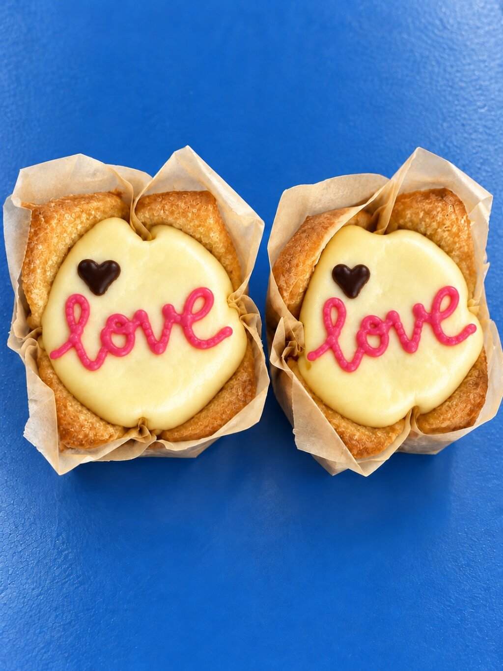 Two muffins with a white topping, the word love in pink and a small dark heart